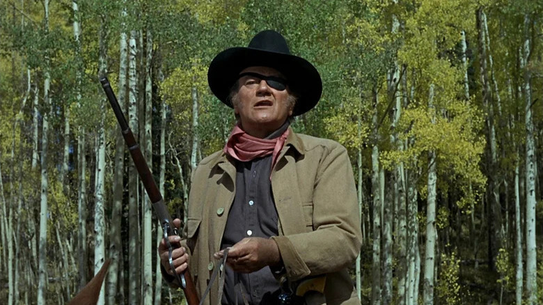 Rooster Cogburn (John Wayne) looks up holding a bridle and rifle in True Grit (1969)