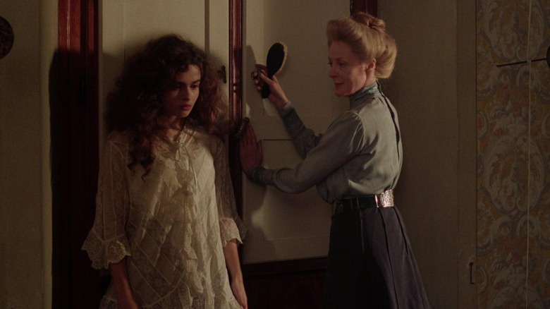 Helena Bonham Carter as Lucy Honeychurch standing next to Maggie Smith as Charlotte Barlett in a dimly-lit bedroom in A Room with a View