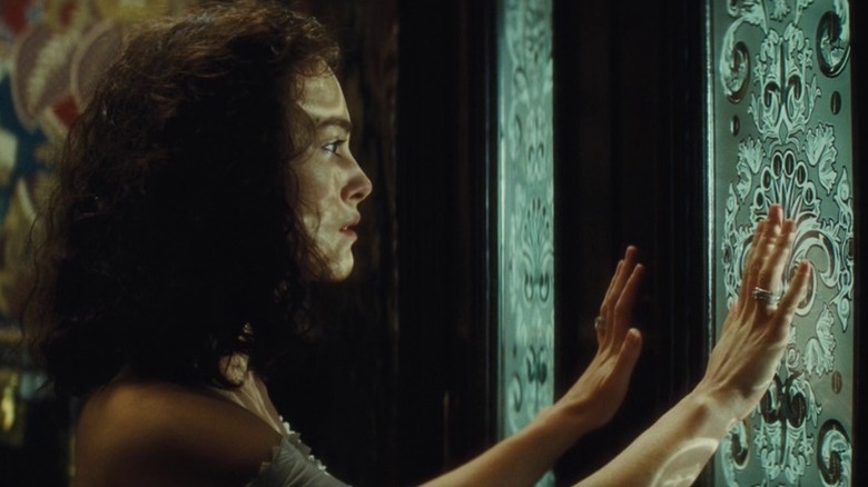 Keira Knightley as Anna Karenina standing with her hands oustretched behind a stained glass door in Anna Karenina