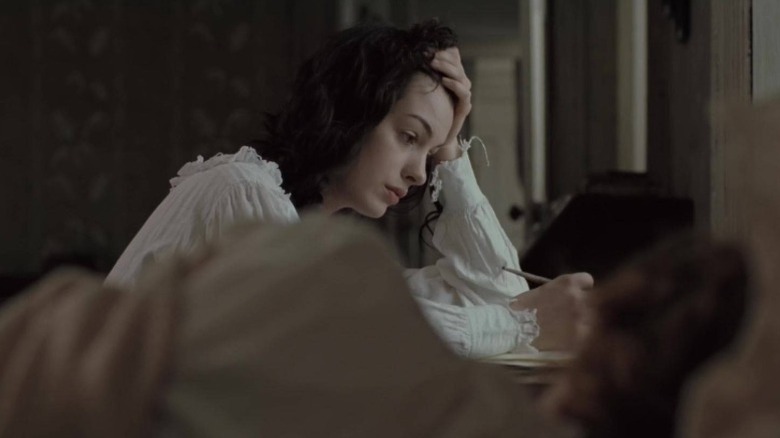 Anne Hathaway as Jane Austen writing at her desk as Anna Maxwell Martin as Cassandra Austen looks on from the bed in Becoming Jane