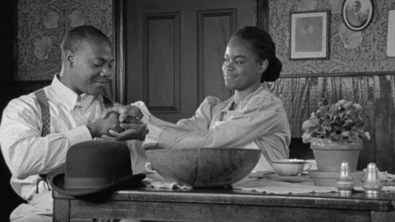Michelle A. Banks as Malindy Brown holding the hand of John Earl Jelks as Arthur Jones while both sit at a table in Compensation