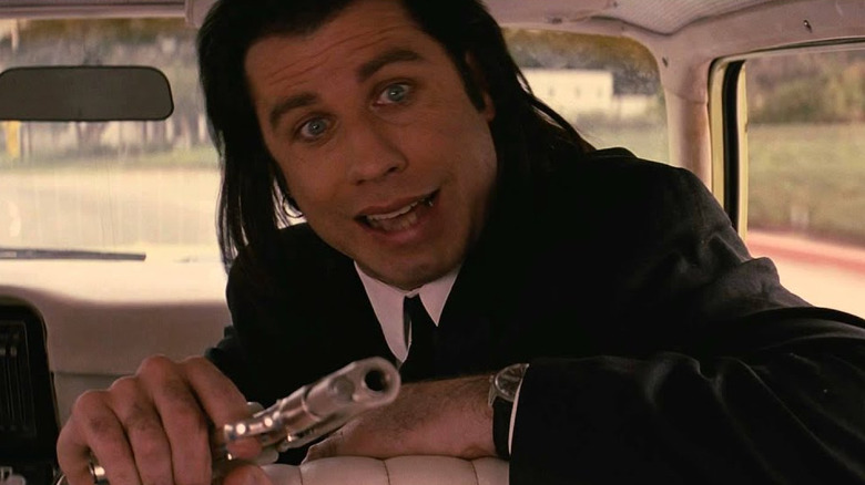 John Travolta as Vincent Vega pointing a gun toward the backseat of a car in Pulp Fiction.