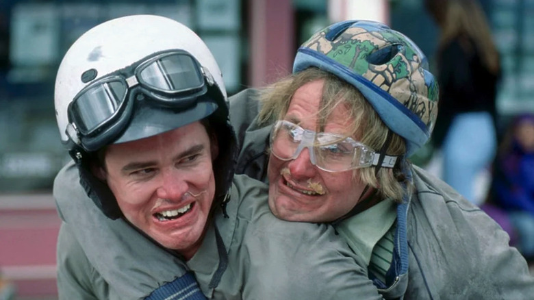 Lloyd Christmas (Jim Carrey) and Harry Dunne (Jeff Daniels) smile with snot on their face while riding a motorized scooter in Dumb and Dumber