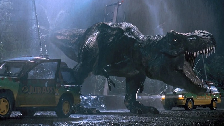 A T-Rex roars between two jeeps on a rainy road in Jurassic Park