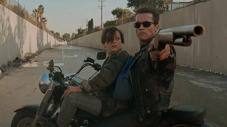 John Connor (Edward Furlong) watches the T-800 (Arnold Schwarzenegger) aim a shotgun while sitting on a motorcycle in Terminator 2: Judgment Day