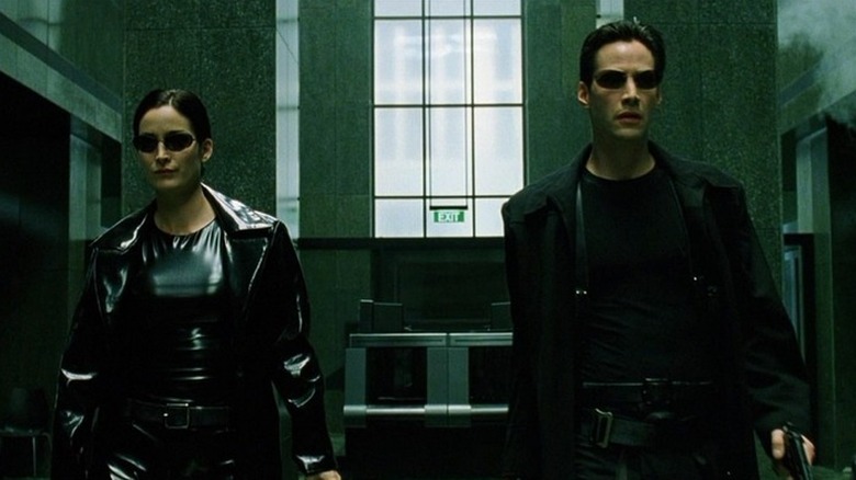 Trinity (Carrie-Anne Moss) and Neo (Keanu Reeves) walk through a lobby holding guns in The Matrix