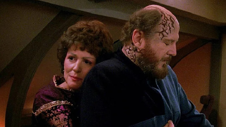 Lwaxana Troi (Majel Barrett) hugs Timicin (David Ogden Stiers) from behind in Star Trek: The Next Generation