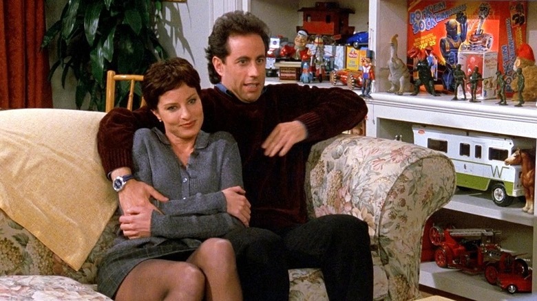 Jerry Seinfeld as Jerry on a couch with Julia Pennington as Celia next to a shelf full of toys in Seinfeld
