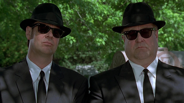 Elwood Blues (Dan Aykroyd) stands next to Mighty Mack McTeer (John Goodman) in their Blues Brothers gear in Blues Brothers 2000