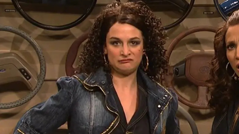 Jenny Slate in a jean jacket with big hoop earrings selling steering wheels in an SNL sketch