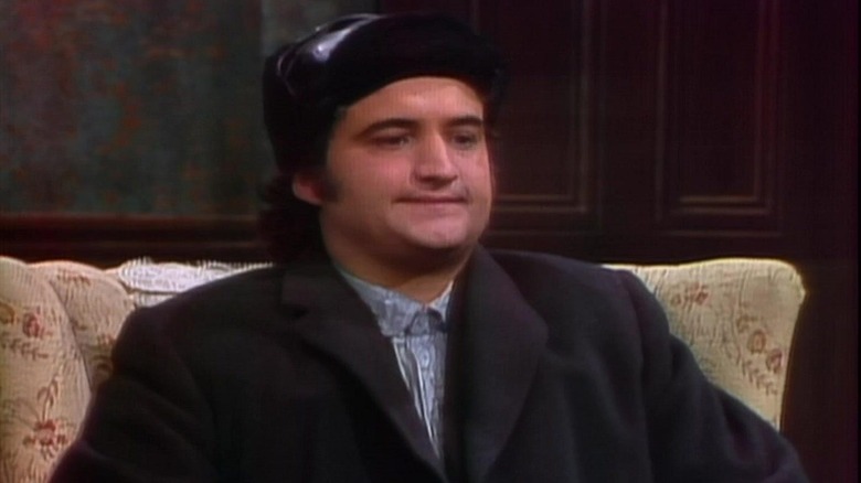 John Belushi as a foreigner sitting in a chair in the Wolverines sketch on SNL