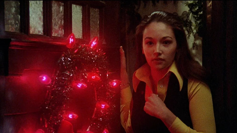 Olivia Hussey as Jess in yellow shirt with hand against door with wreath and red lights on it in Black Christmas