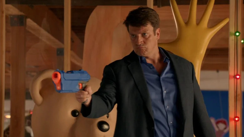 Richard Castle (Nathan Fillion) stoically aims a dart gun in Castle