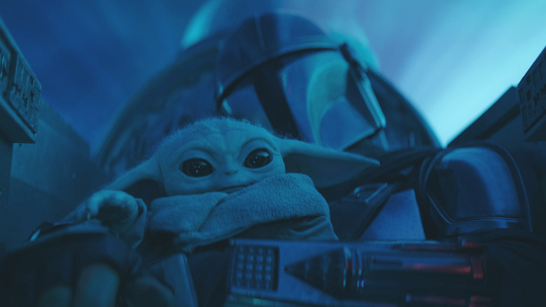 Grogu sitting on Mando's lap in the cockpit of his ship in The Mandalorian