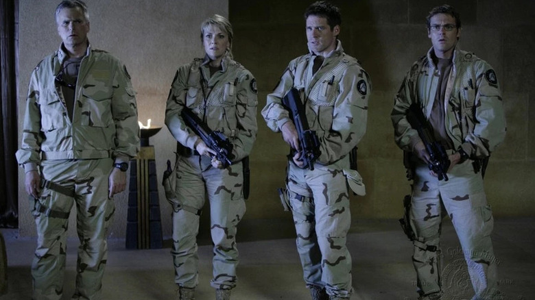 Four people standing in military garb with guns: Jack O'Neill (Richard Dean Anderson), Samantha Carter (Amanda Tapping), Cameron Mitchell (Ben Browder), and Daniel Jackson (Michael Shanks) in Stargate: Continuum