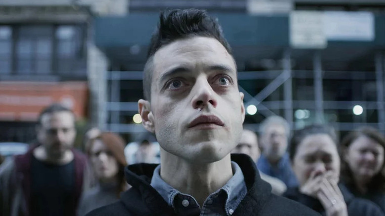 Rami Malek standing in crowd of people looking up 