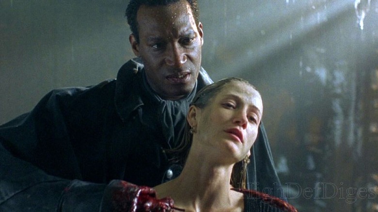 Candyman stands behind a woman and holds a hooked hand to her throat.