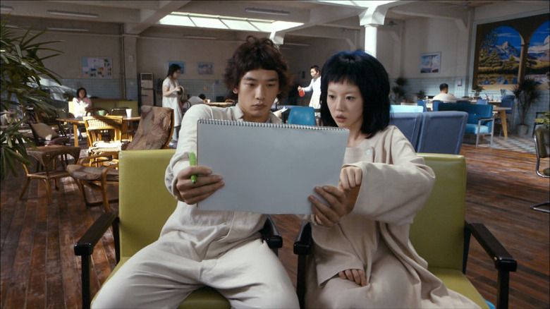 Young-goon and Il-soon sitting on chairs looking at sketchbook in I'm a Cyborg, But That's OK