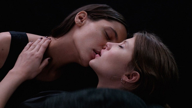 Anja leaning over to kiss Thelma with black background in Thelma