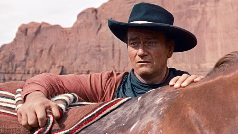 John Wayne as Ethan Edwards leans on a horse in The Searchers