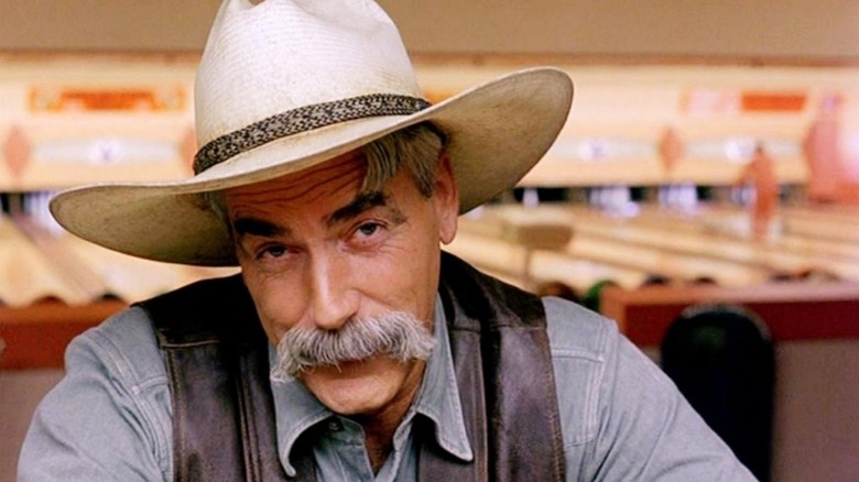 Sam Elliott as The Stranger sits in a bowling alley in The Big Lebowski