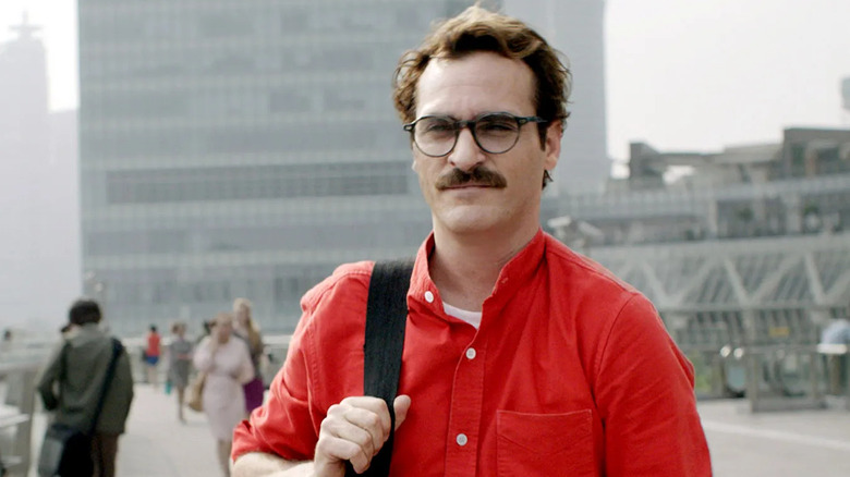 Joaquin Phoenix as Theodore Twombly walks smiling through a city street in Her.