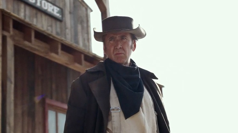 Nicolas Cage as Colton Briggs looking ahead next to old western store in The Old Way