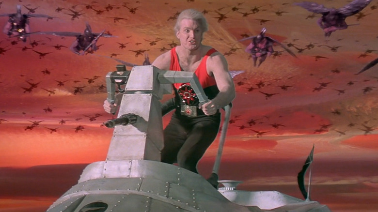 Sam J. Jones as Flash Gordon on a flying vehicle being pursued by flying warriors