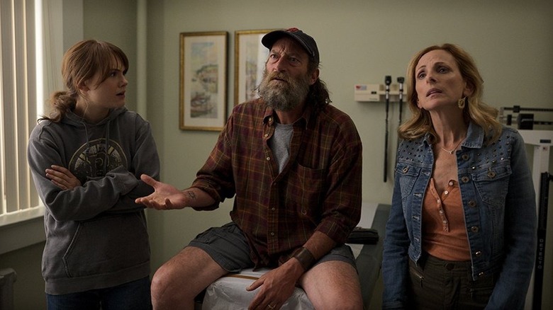 Emilia Jones as Ruby standing next to Troy Kotsur as Frank who is sitting on an exam room table next to Marlee Matlin as Jackie in Coda