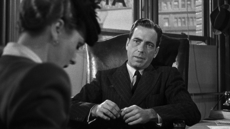 Humphrey Bogart as Sam Spade speaks with Mary Astor as Bridgid O'Shaughnessy at his desk in his office in The Maltese Falcon