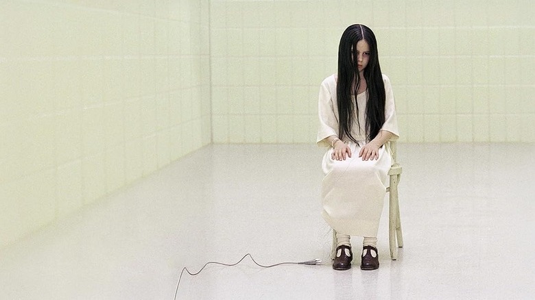 Daveigh Chase as Samara sitting in an all-white room in a white dress with long dark hair in The Ring