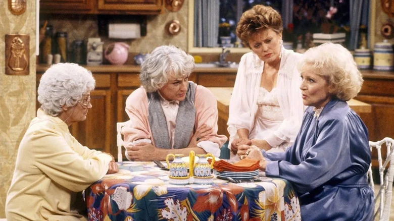 Estelle Getty, Bea Arthur, Rue McClanahan, and Betty White as Sophia Petrillo, Dorothy Zbornak, Blanche Devereaux, and Rose Nylund at their kitchen table listening to Rose tell a story in The Golden Girls