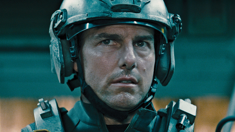 Tom Cruise as Major William Cage in Edge of Tomorrow, wearing his mech helmet and staring off at something past the frame.