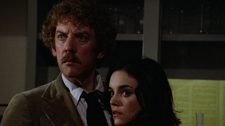 Donald Sutherland as Matthew Bennell and Brooke Adams as Elizabeth Driscoll in Invasion of the Body Snatchers, standing next to each other in a room as they both look off with concern in the same direction toward the left side of the frame.