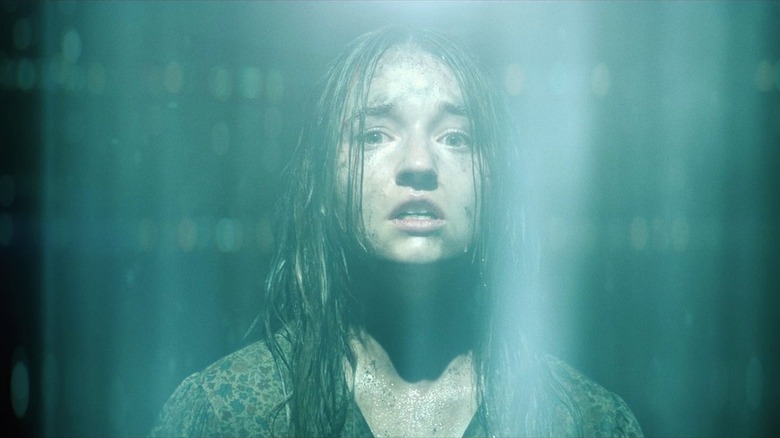 Kaitlyn Dever as Brynn in No One Will Save You, looking dirty and disheveled as she stands under a beam of light and looks into the camera