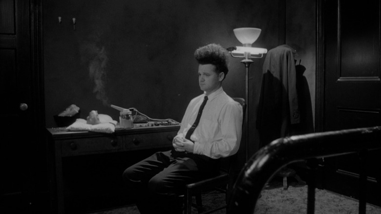 Jack Nance as Henry Spencer in Eraserhead, sitting in his apartment with his mutant baby wrapped up on the table under an air purifier.