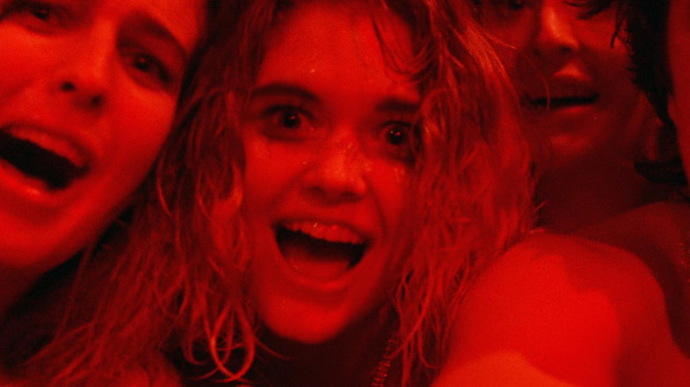 Patrice Jennings as Jenny Whitney and Connie Danese as Nan Whitney in Society, packed tightly into a close-up with a larger group and bathed in red light as they look on cackling.