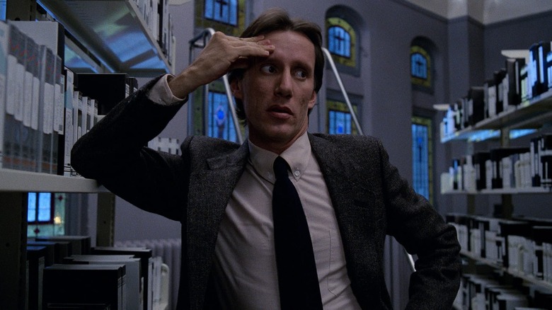James Woods as Max Renn in Videodrome, standing amid a collection of videotapes and touching his forehead.