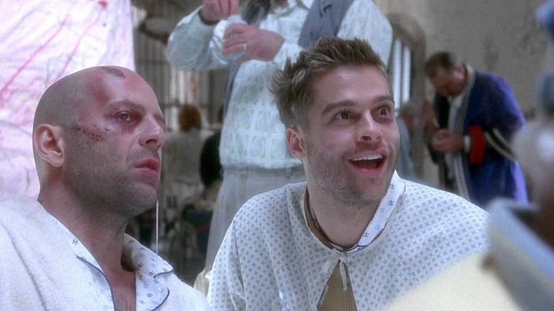 Bruce Willis as James Cole sitting next to a manic-looking Brad Pitt as Jeffrey Goines in 12 Monkeys.