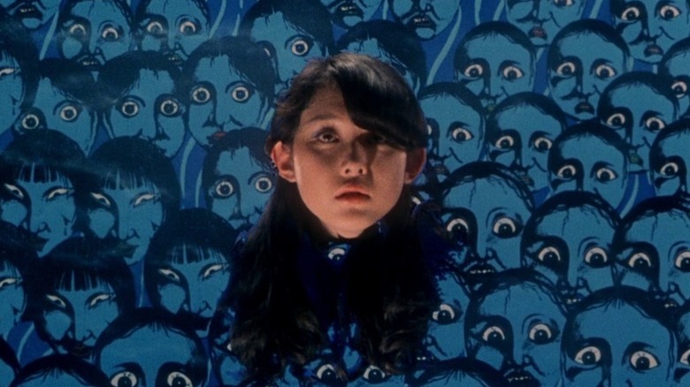 The disembodied head of Miki Jimbo as Kung Fu in front of a background of blue painted faces in House