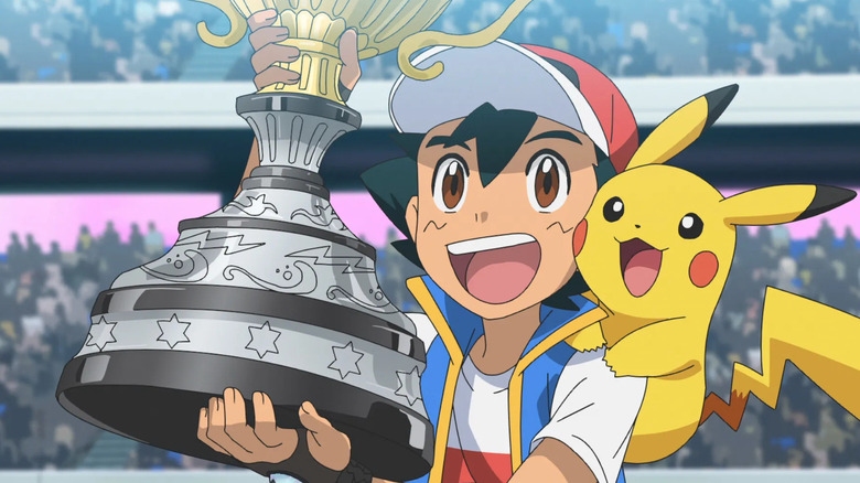 Ash smiling holding a championship trophy with Pikachu on his shoulder in Pokemon Journeys
