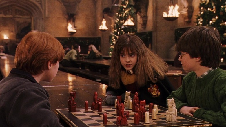 Ron, Hermione, and Harry sit around a dining table playing chess at Christmas in Harry Potter and the Sorcerer's Stone