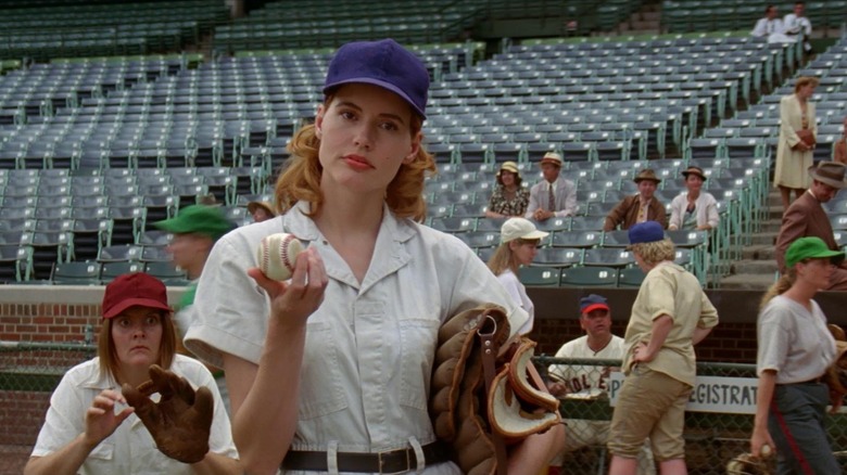Geena Davis as Dorothy "Dottie" Hinson and Megan Cavanagh as Marla Hooch in A League of Their Own, with Dorothy in the foreground holding a baseball and mitt as Marla squats behind her and seemingly prepares for a pitch.