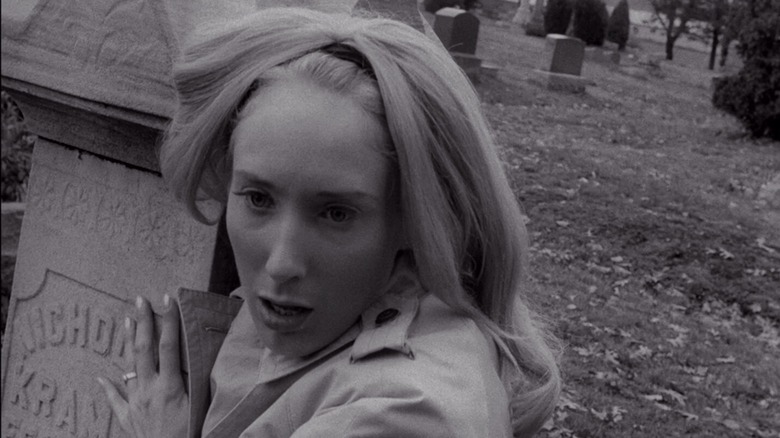 Judith O'Dea as Barbra in Night of the Living Dead, gripping a gravestone as she looks off at something in shock.