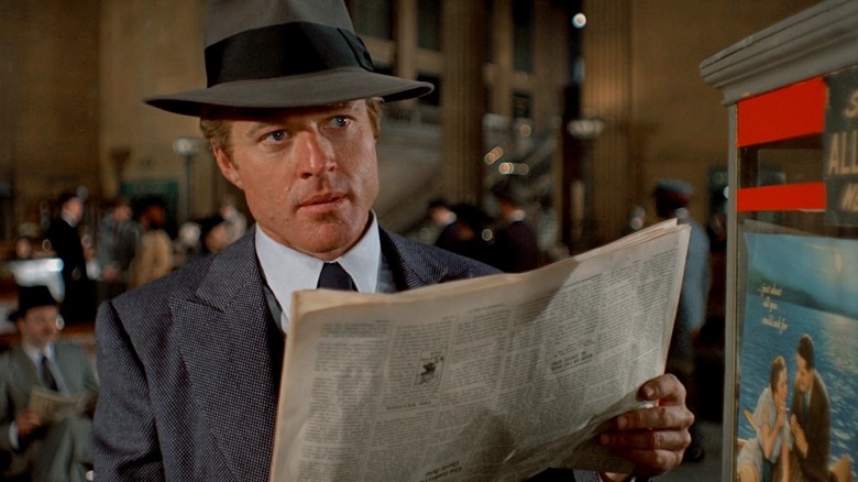 Robert Redford as Johnny Hooker in The Sting, wearing a suit and hat and looking over a newspaper in his hands.