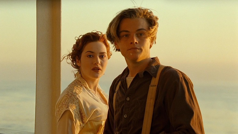Leonardo DiCaprio as Jack Dawson and Kate Winslet as Rose DeWitt Bukater in Titanic, standing together against the backdrop of a dusk-set sky and looking off past the camera.