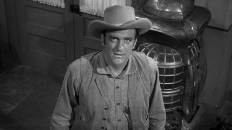 Matt Dillon (James Arness) looks up from standing next to a stove in Gunsmoke