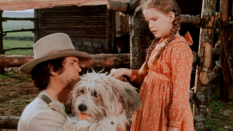 Charles Ingalls (Michael Landon) holds a dog next to a fence while speaking to Laura Ingalls (Melissa Gilbert) in Little House on the Prairie
