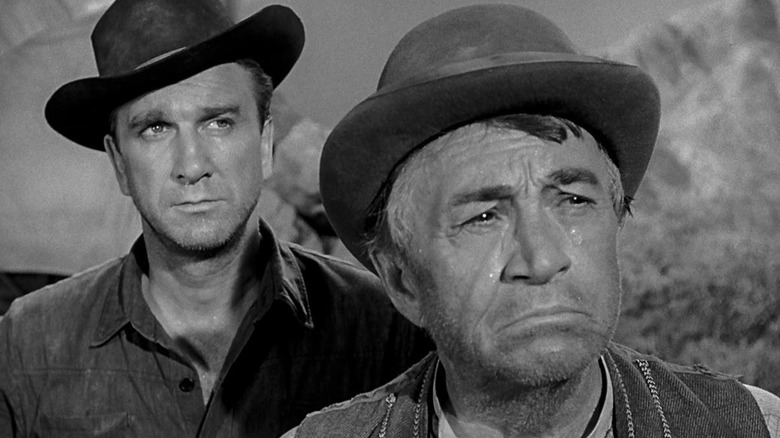 Jeremy Dow (Leslie Nielsen) stands somberly behind a crying Amos Billings (Paul Fix) in Wagon Train