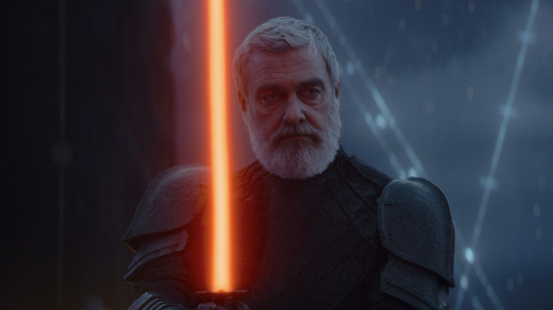 Ray Stevenson as Baylan Skoll with a beard wearing armour and weilding a red-orange/blood orange lightsaber in Star Wars: Ahsoka